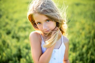 close-up portrait of cute little child in white dress posing in green field and looking at camera