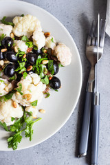 Fresh vegetable salad with cauliflower, olives, parsley and pine nuts in a grey plate on a grey stone background. Healthy food concept