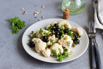 Fresh vegetable salad with cauliflower, olives, parsley and pine nuts in a grey plate on a grey stone background. Healthy food concept