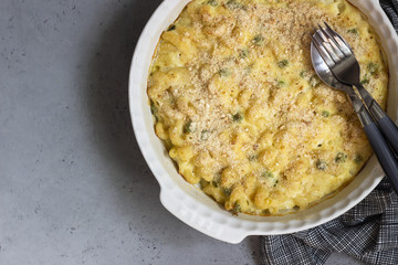Homemade pasta casserole with fish and green pea in bechamel sauce in a baking dish on a light slate, stone or concrete background. Copy space for text.