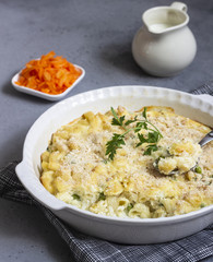 Homemade pasta casserole with fish and green pea in bechamel sauce in a baking dish on a light slate, stone or concrete background. Copy space for text.