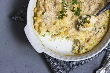 Homemade pasta casserole with fish and green pea in bechamel sauce in a baking dish on a light slate, stone or concrete background. Copy space for text.
