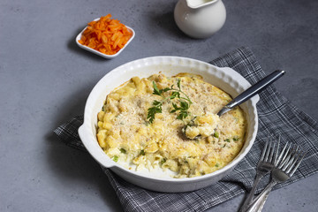Homemade pasta casserole with fish and green pea in bechamel sauce in a baking dish on a light slate, stone or concrete background. Copy space for text.
