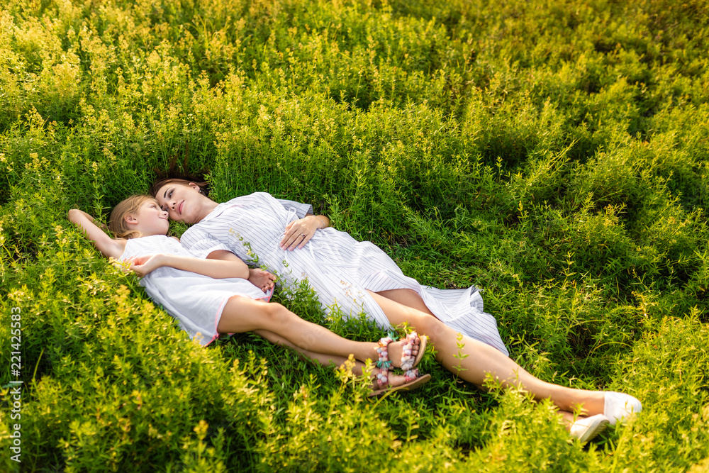 Wall mural beautiful mother and daughter relaxing while lying in flowery meadow