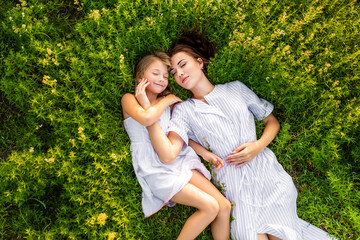 top view of mother and daughter relaxing while lying in flowery meadow
