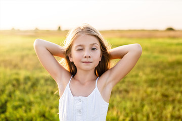 adorable little child winking at camera on green field under sunset rays