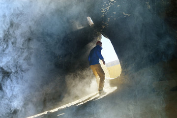entrance to the cave, a male traveler stands in the rays of light at the exit of the cave,...