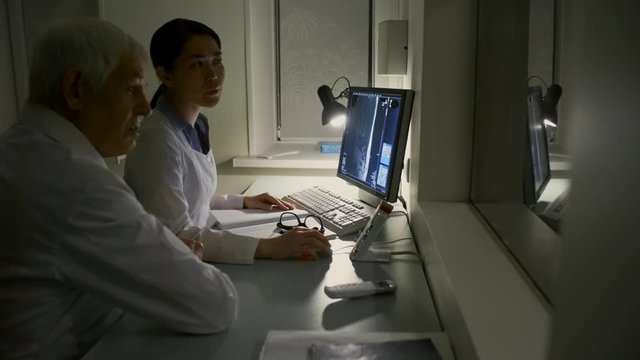 Professional female doctor using computer while performing MRI exam and discussing image on computer screen with senior male colleague