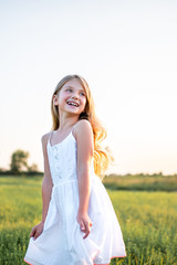 Fototapeta na wymiar happy little child in white dress posing on field on sunset