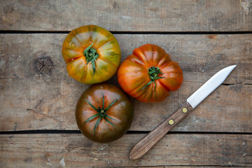 Reife farbige Tomaten zusammen mit einem Messer auf einem alten Holzuntergrund
