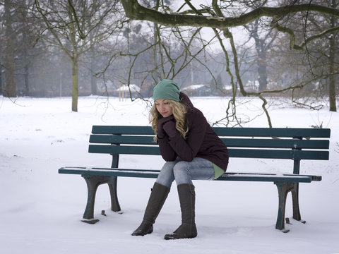 Woman Sitting Alone On Snow Covered Park Bench With Winter Depression