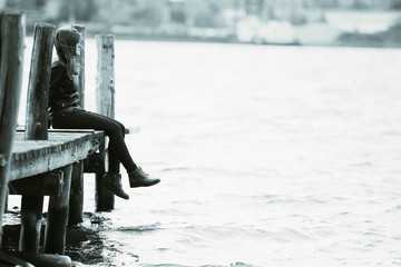 Young adult woman sitting on a wooden jetty on the river