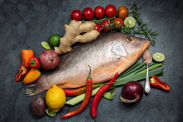 Fresh raw red snapper fish with spices, herbs and vegetables for cooking on dark background. Top view.