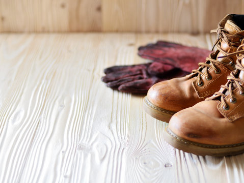 Yellow leather used work boots and protective gloves on wooden background closeup. Place for text