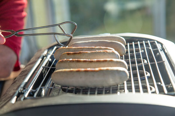 Mann grillt und dreht Bratwurst auf elektronischen Grill mit Grillzange aus Metall