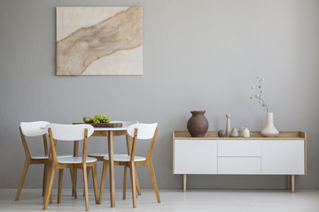 Real photo of wooden table and four chairs standing in light grey dining room interior with modern...