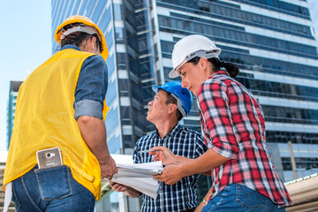 Three industrial engineer wear safety helmet engineering working and talking with drawings inspection on building outside. Engineering tools and construction concept. With copy space
