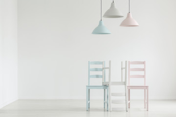 Lamps above pastel chairs in white empty living room interior with copy space on the wall. Real photo