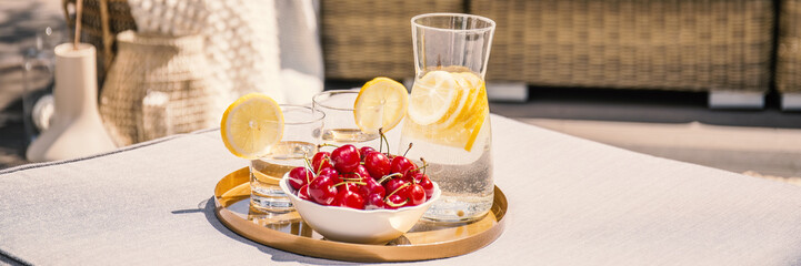 Cherries and water with lemon on table on terrace during summer. Real photo