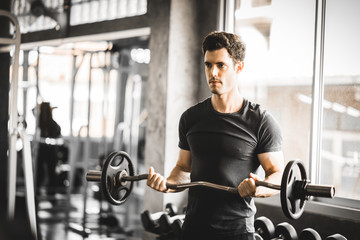 Plakat Fit caucasian handsome young man and big muscle in sportswear. Young man holding dumbbell during an exercise class in a gym. Healthy sports lifestyle, Fitness concept.