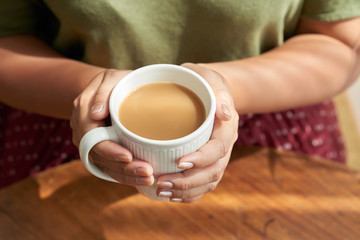 From above shot of crop lady holding mug of aromatic coffee over table in nice cafe