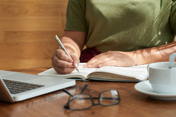 Anonymous female writing in notebook while sitting at table in good cafe