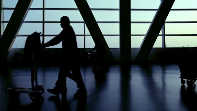 Silhouette of travelers passengers in airport transit terminal walking with luggage baggage going traveling