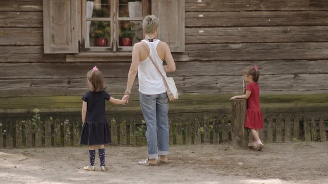 young mother walks with her daughters in a rural park and watches old houses