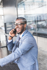 black man businessman in a business suit, expensive watch and glasses talking on the phone, decides business matters against the backdrop of a modern city to work