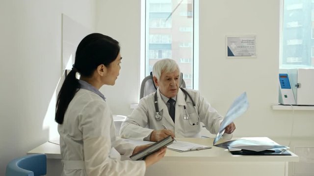 Female Asian doctor and senior male practitioner discussing chest x-ray image while working together in clinic