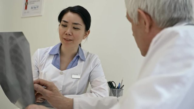 Cheerful Asian female doctor smiling and discussing x-ray image with senior colleague in clinic