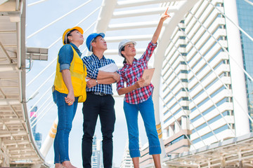 Three industrial engineer standing and looking to right side wear safety helmet with holding inspection and digital tablet on building outside. Engineering tools and construction concept.