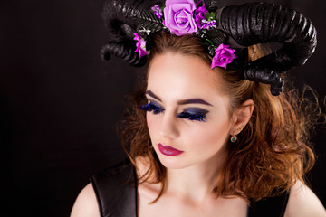 Model with fashion make-up and horns on the head on a black background