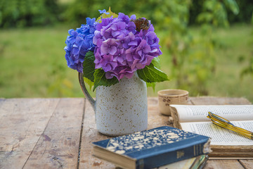 Old opened book, glasses, cup of coffee and bouquet of blue hydrangea on vintage table in the garden