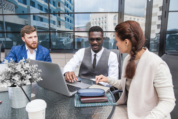 Group of happy diverse male and female business people team in formal gathered around laptop computer in bright office against the background of a glass building
