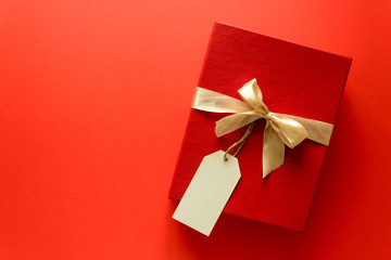 Top view on red Christmas gift box decorated with ribbon on red paper background. New Year, holidays and celebration decorations concept. Copy space. Flat lay. Mock-up