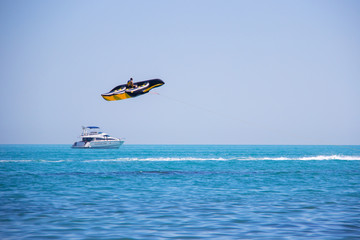Young man in lifejackets have fun and ride a large black and yellow flying banana boat water attraction in the sea on the background clear sky.