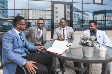 Group of happy diverse male and female business people team in formal gathered around laptop computer in bright office against the background of a glass building