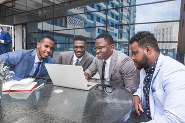 Group of happy diverse male and female business people team in formal gathered around laptop computer in bright office against the background of a glass building