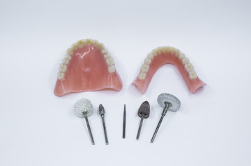 A set of dentures and some dental grinding and polishing tools on a white background.