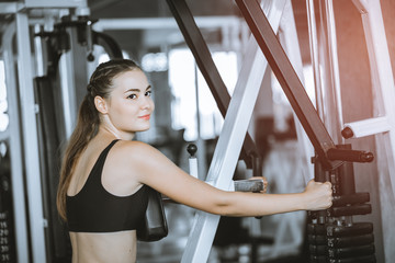 Fototapeta na wymiar Fit beautiful young woman exercise workout on machine in gym. Glad smiling girl is enjoy with her training process. Concept of fitness, Healthy, Sport, Lifestyle