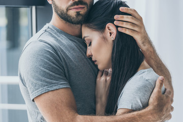 cropped shot of bearded man hugging and supporting young sad woman - obrazy, fototapety, plakaty