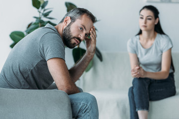 upset middle aged man sitting on couch and girlfriend sitting behind