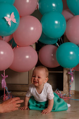 Obraz premium the child cries, gets angry, a little girl, a child, sits on the floor and cries, wrinkled her nose, near the balloons, a holiday. birthday, turned a year old. resentment, disappointment