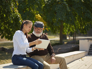 Help someone you love. Portrait of young smiling girl sitting with grandfather and laptop against city park. community and family lifestyle concept