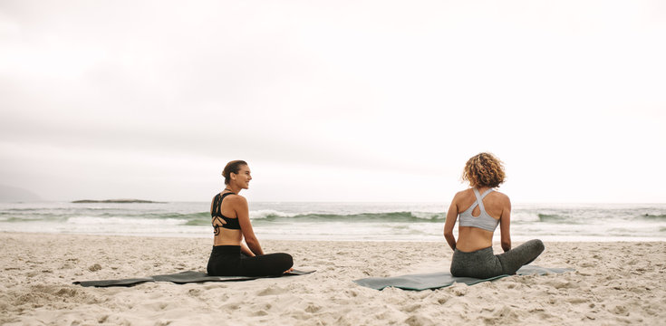 Two women doing yoga sitting at the beach