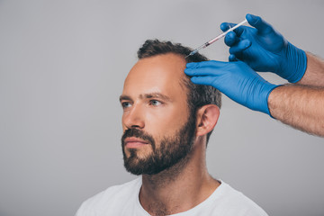 cropped shot of doctor with syringe giving injection to man with alopecia looking away isolated on grey