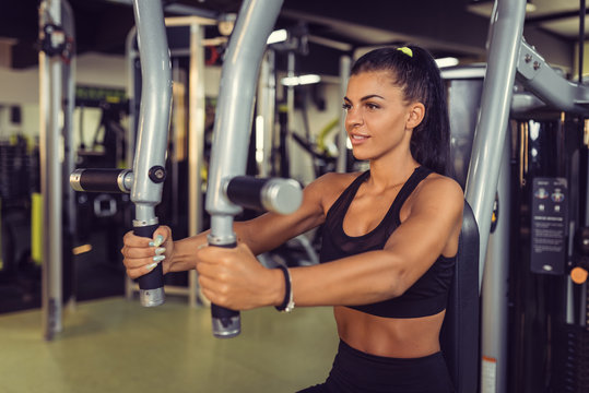 Young woman training upper body using fly machine