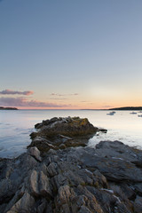 Boats sitting at anchor in Kettle Cove, Main during sunset with a rocky peninsula in the foreground.