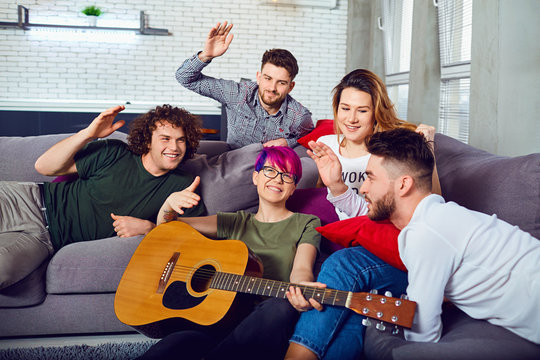 Cheerful group of friends with a guitar at a party in a room.